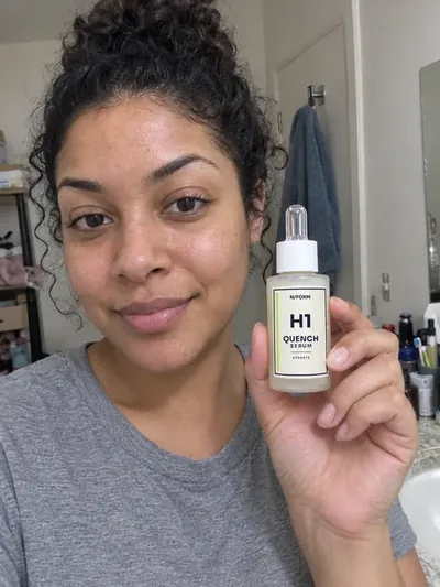 A woman holding the H1 Quench Serum bottle in a bathroom