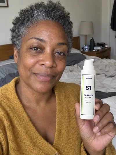 A woman holding the S1 Barrier Cream jar in a bedroom