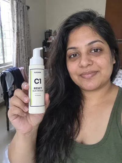 A woman holding the C1 Reset Cleanser bottle by a window