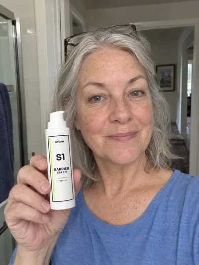 A woman holding the S1 Barrier Cream jar in a doorway